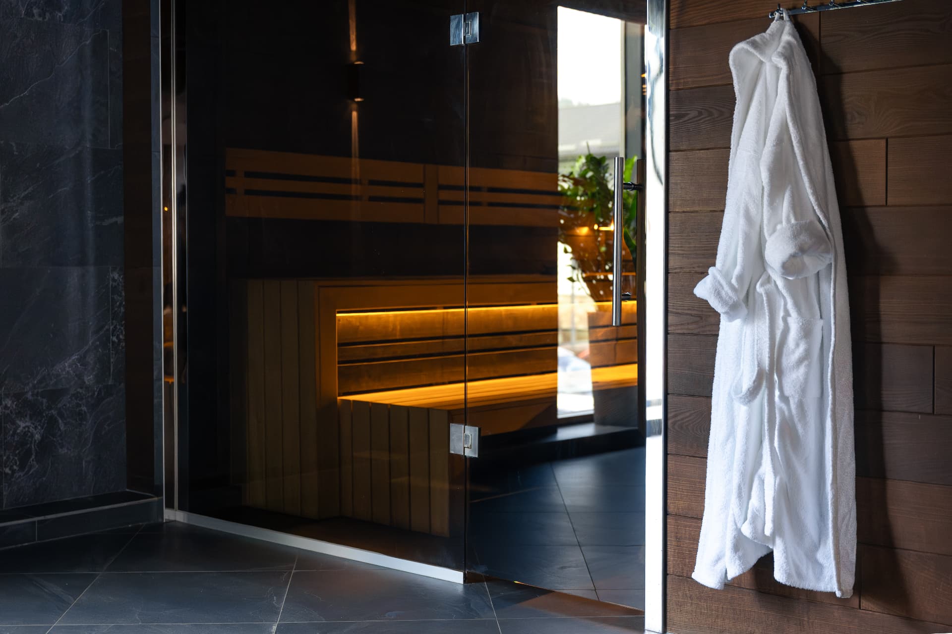 White robe hanging on a timber wall beside a glass-fronted sauna