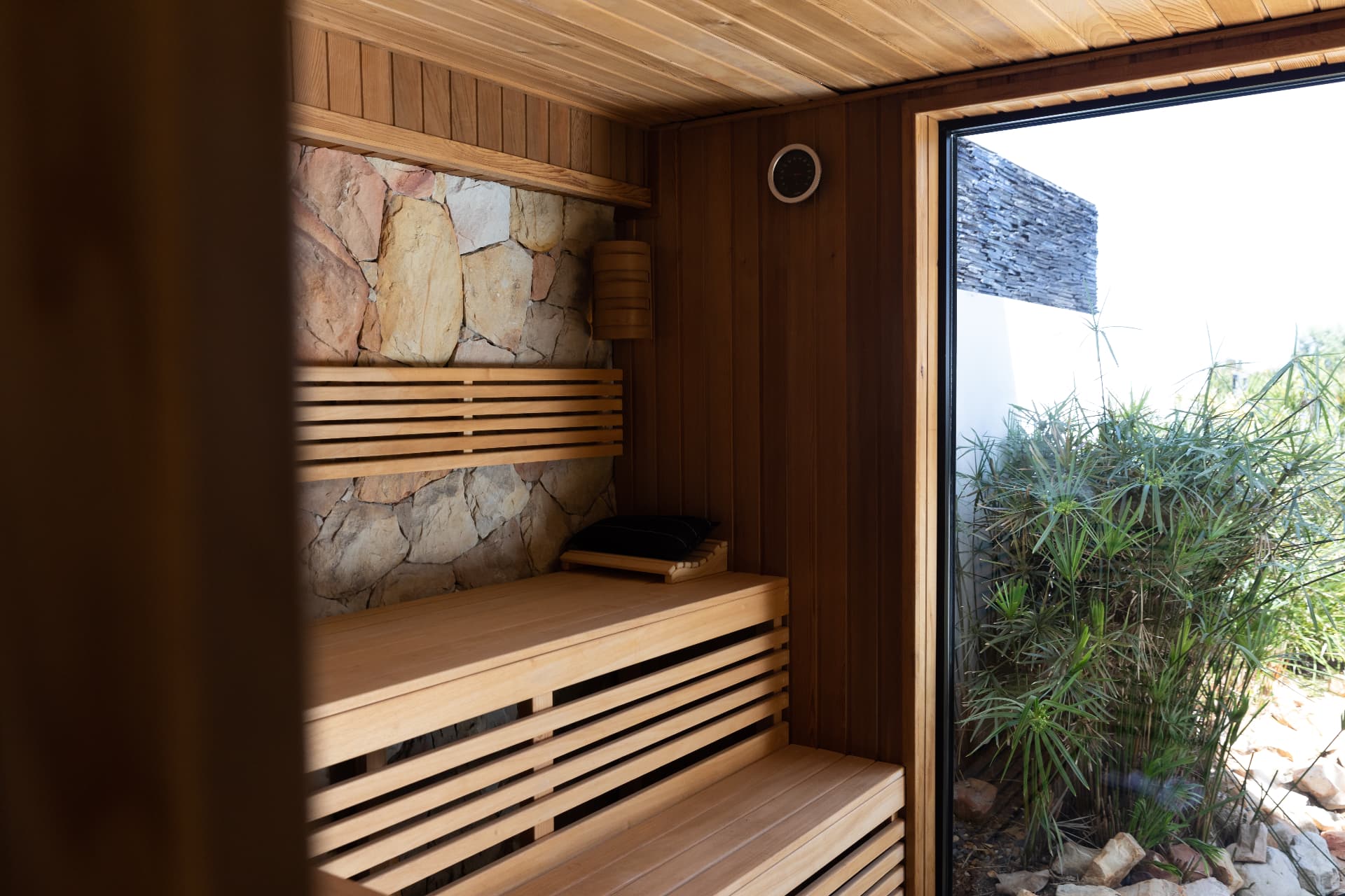 Cedar sauna interior with slatted benches and a glazed door opening to planting