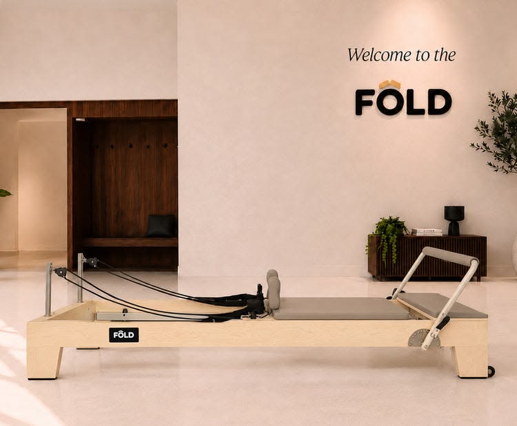 Wooden FÔLD reformer with cream upholstery in a studio beneath a Welcome to the FÔLD sign