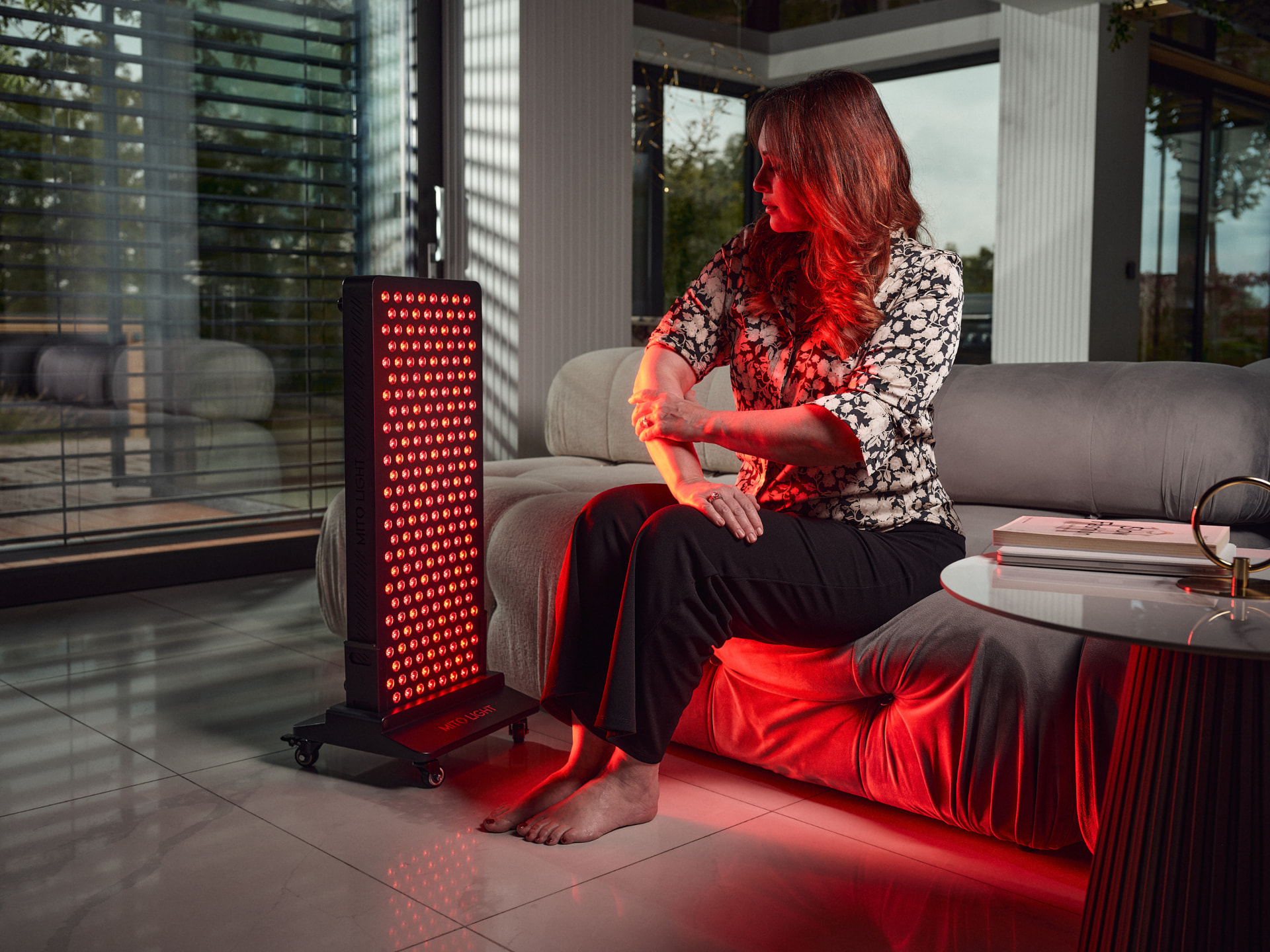 Woman using a full-height MITO LIGHT red light therapy panel in a modern living room